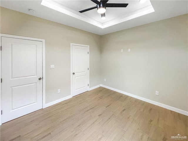 unfurnished room with a ceiling fan, a raised ceiling, light wood-style flooring, and baseboards