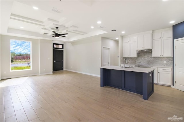 kitchen with coffered ceiling, a sink, under cabinet range hood, white cabinetry, and backsplash