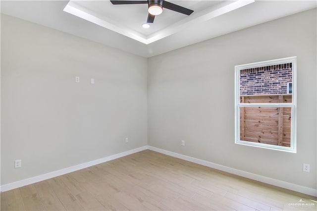 empty room with a tray ceiling, recessed lighting, ceiling fan, wood finished floors, and baseboards