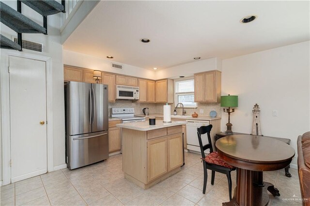 kitchen with light brown cabinets, white appliances, a kitchen island, and sink