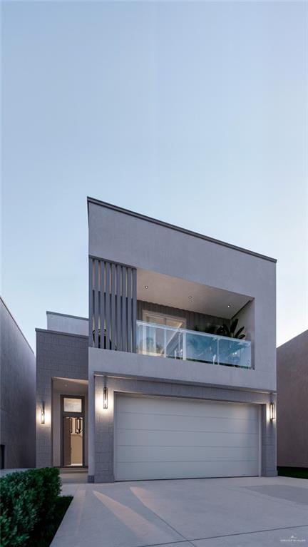 contemporary house with a balcony, stucco siding, an attached garage, and concrete driveway