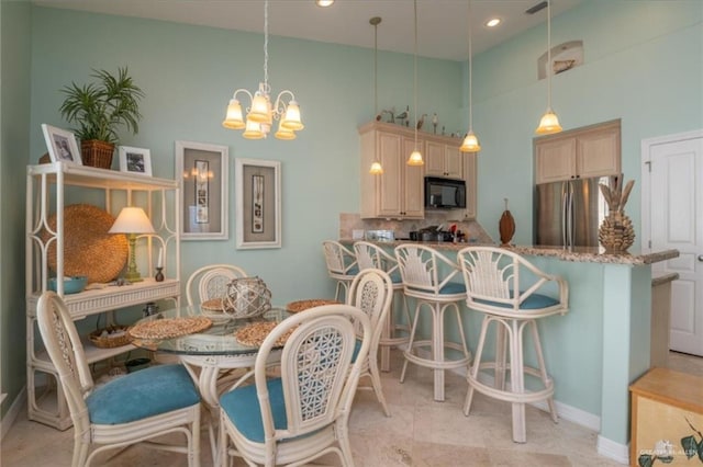 kitchen featuring stainless steel refrigerator, hanging light fixtures, a notable chandelier, backsplash, and a breakfast bar