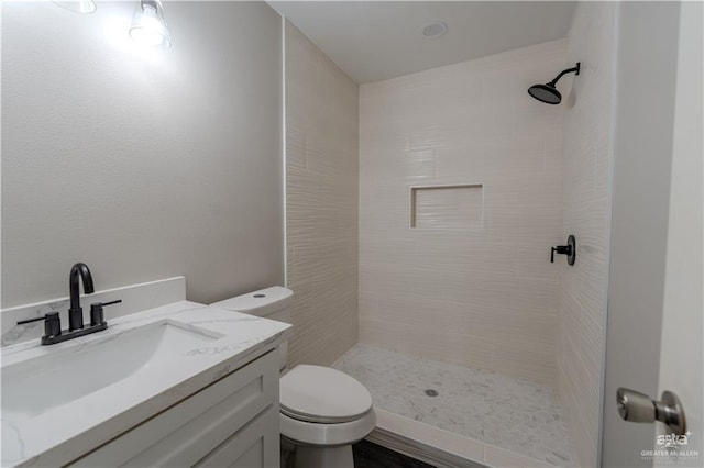 bathroom featuring a tile shower, vanity, and toilet