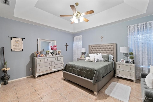 tiled bedroom with ceiling fan and a tray ceiling