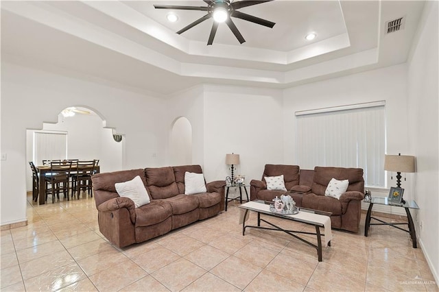 tiled living room featuring ceiling fan and a tray ceiling