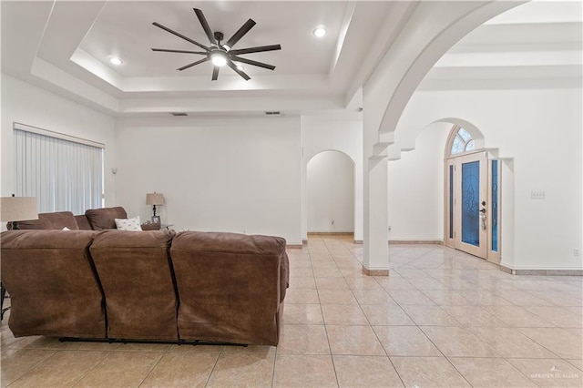 living room featuring ceiling fan, light tile patterned flooring, and a tray ceiling