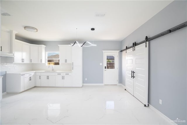 kitchen featuring decorative light fixtures, sink, white cabinetry, and a barn door