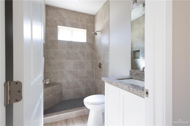 bathroom featuring a tile shower, vanity, and toilet