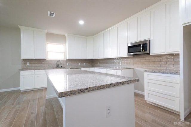 kitchen featuring light wood-type flooring, white cabinetry, a kitchen island, and light stone counters