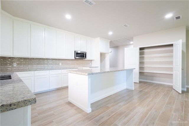 kitchen with white cabinets, decorative backsplash, a center island, and light stone counters