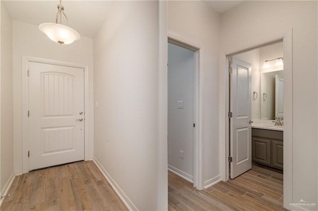 hallway featuring light wood-style flooring, baseboards, and a sink