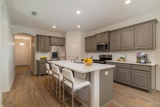 kitchen with arched walkways, appliances with stainless steel finishes, a kitchen island with sink, light countertops, and a sink