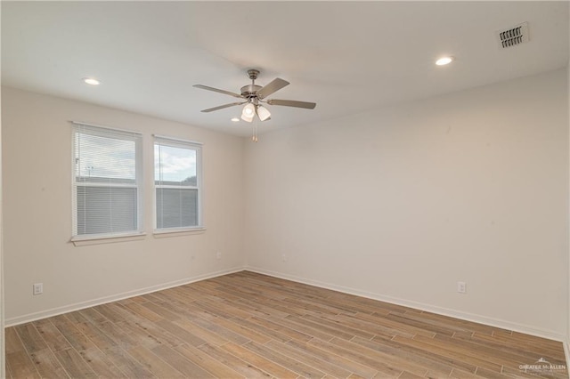 empty room featuring a ceiling fan, visible vents, light wood-style flooring, and baseboards