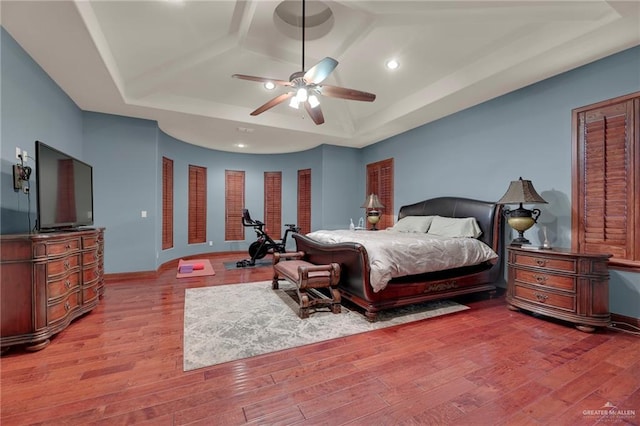 bedroom with a raised ceiling, ceiling fan, and light wood-type flooring