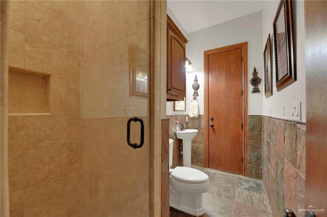 bathroom featuring toilet, a shower with shower door, and tile walls