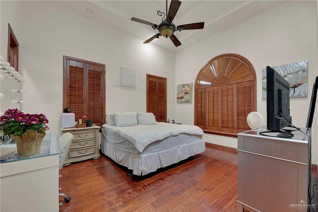 bedroom with ceiling fan, a high ceiling, and dark hardwood / wood-style floors