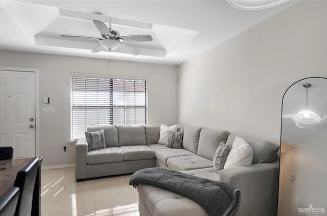 living room with a tray ceiling, ceiling fan, and light tile patterned flooring