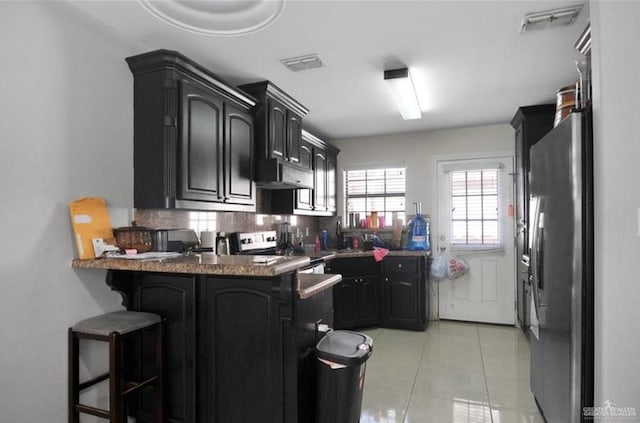 kitchen featuring tasteful backsplash, a kitchen breakfast bar, kitchen peninsula, light tile patterned floors, and appliances with stainless steel finishes