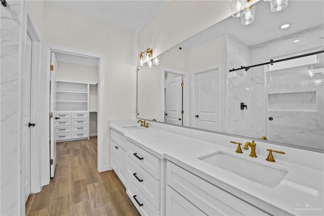 full bathroom featuring double vanity, wood finished floors, a sink, and a marble finish shower