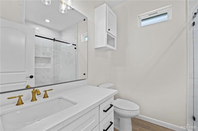 bathroom with toilet, a shower stall, vanity, wood finished floors, and baseboards