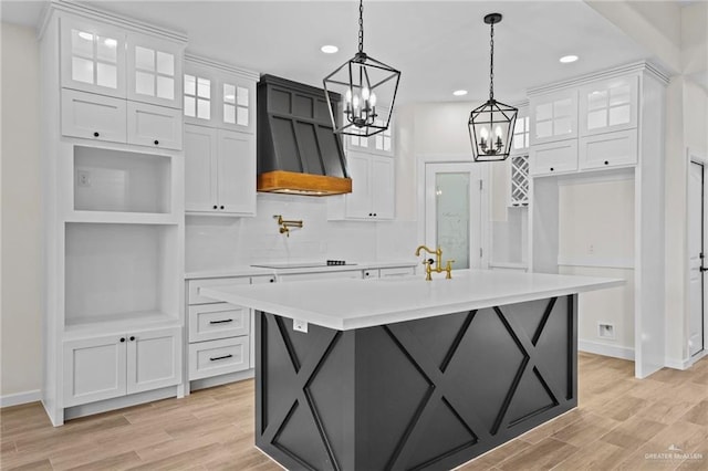 kitchen featuring light wood finished floors, light countertops, white cabinets, an island with sink, and premium range hood