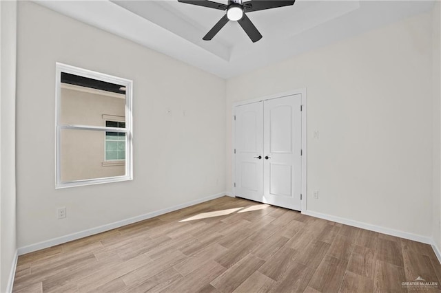 unfurnished bedroom featuring baseboards, a ceiling fan, wood finished floors, a tray ceiling, and a closet