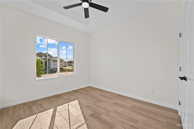 unfurnished room featuring baseboards, a tray ceiling, a ceiling fan, and light wood-style floors