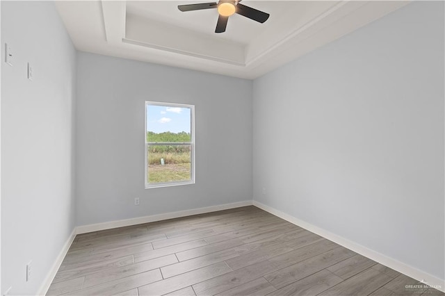 unfurnished room featuring a raised ceiling, ceiling fan, and light hardwood / wood-style flooring