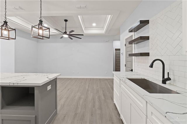 kitchen featuring sink, hanging light fixtures, a raised ceiling, light stone counters, and white cabinets