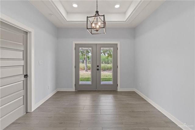 entryway featuring a raised ceiling, french doors, a chandelier, and wood-type flooring