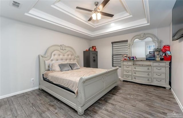 bedroom with ceiling fan, a raised ceiling, and wood-type flooring