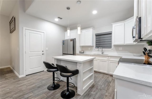 kitchen with a center island, white cabinets, hanging light fixtures, sink, and appliances with stainless steel finishes