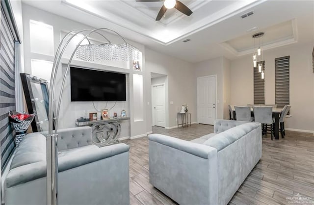 living room featuring a raised ceiling, ceiling fan, and light hardwood / wood-style flooring