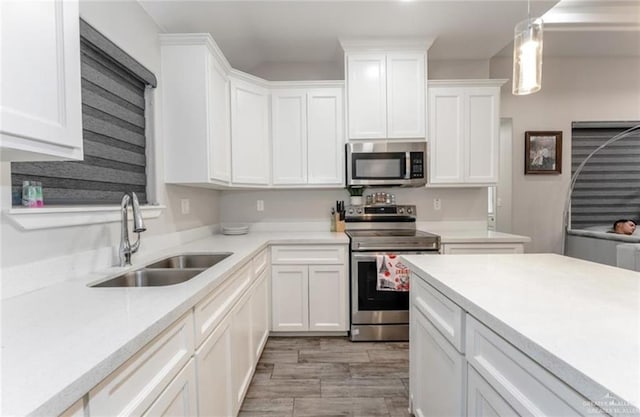 kitchen with sink, light hardwood / wood-style flooring, appliances with stainless steel finishes, decorative light fixtures, and white cabinetry