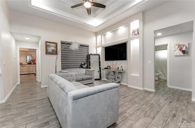 living room with a tray ceiling, ceiling fan, and light hardwood / wood-style floors