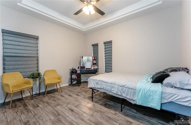 bedroom featuring ceiling fan, wood-type flooring, and a tray ceiling