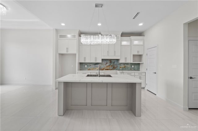 kitchen with sink, a kitchen island with sink, white cabinets, and light stone counters