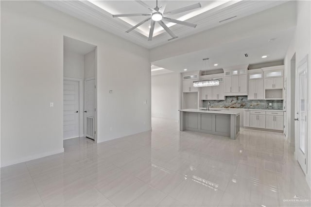 kitchen featuring a kitchen island with sink, hanging light fixtures, sink, tasteful backsplash, and ceiling fan