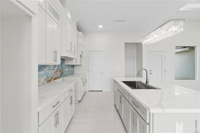 kitchen with light stone counters, white cabinets, backsplash, sink, and a kitchen island with sink