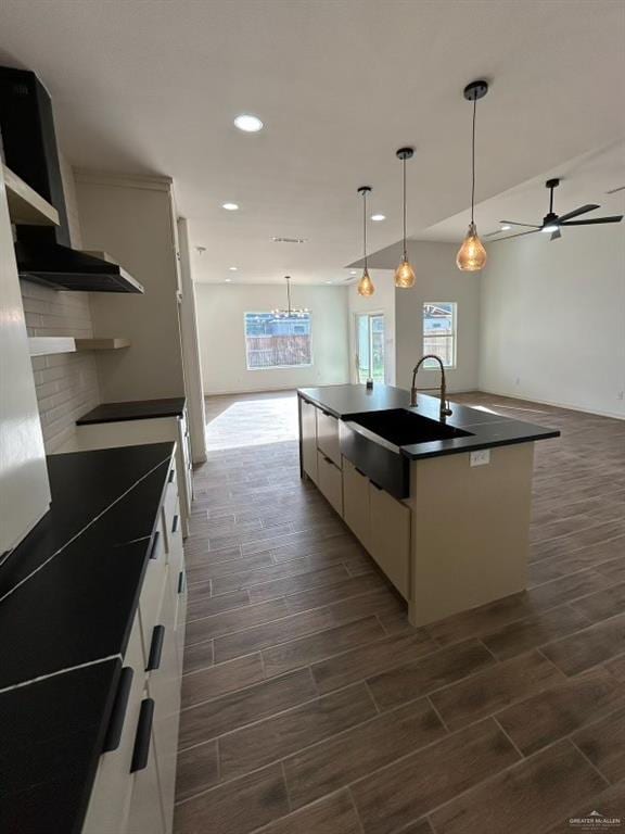 kitchen featuring a center island with sink, white cabinets, dark countertops, open floor plan, and a sink