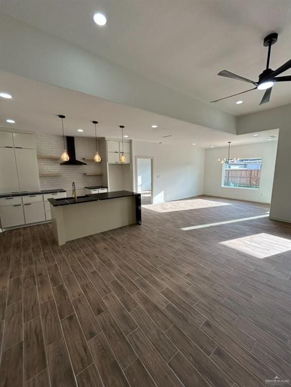 kitchen featuring dark countertops, wood tiled floor, open floor plan, white cabinetry, and wall chimney range hood