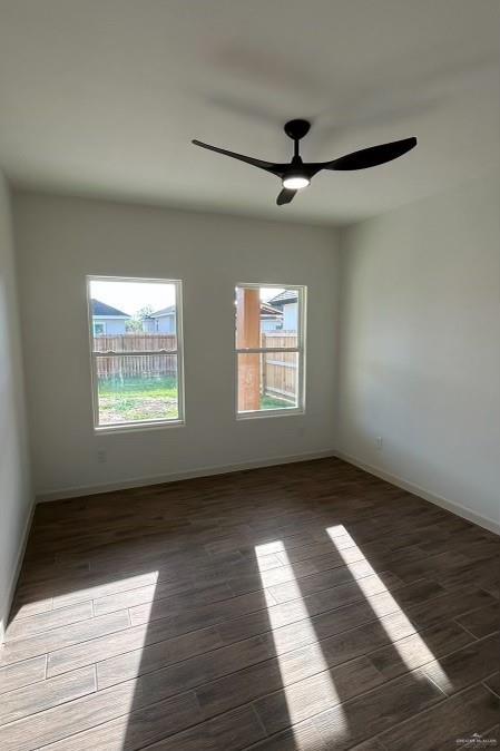 empty room featuring dark wood-style floors, baseboards, and a ceiling fan