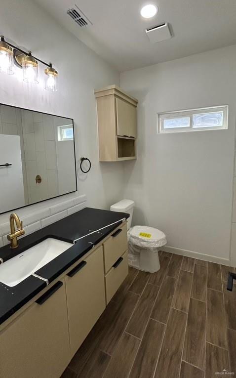 full bathroom with toilet, wood finish floors, vanity, visible vents, and baseboards