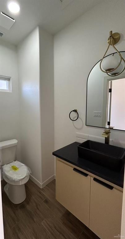 bathroom with toilet, wood finished floors, vanity, and baseboards