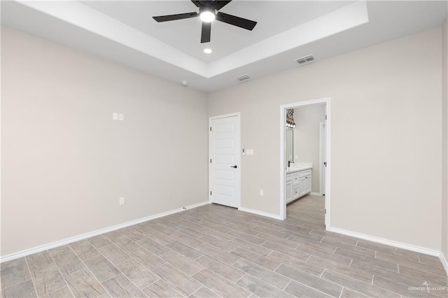 unfurnished bedroom featuring ceiling fan, ensuite bath, and a raised ceiling