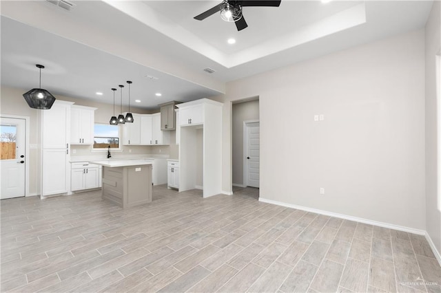 kitchen with hanging light fixtures, ceiling fan, a raised ceiling, a center island, and white cabinetry