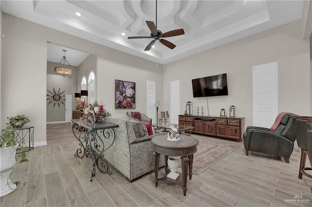 living room with light wood-type flooring, coffered ceiling, ceiling fan with notable chandelier, crown molding, and a high ceiling