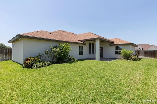 rear view of property with stucco siding, a yard, and fence