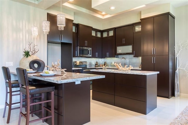 kitchen with backsplash, dark brown cabinetry, appliances with stainless steel finishes, and a kitchen island with sink