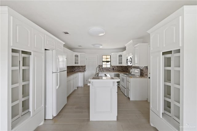2216 Fairmont Ave, Mcallen, TX 78504 - kitchen featuring white appliances, a center island with sink, decorative backsplash, and glass insert cabinets